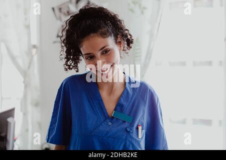 Smiling nurse with curly hair looking away in hospital Stock Photo