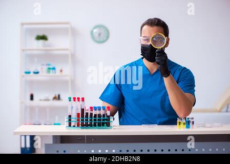 Young male biochemist testing blood samples in pandemic concept Stock Photo