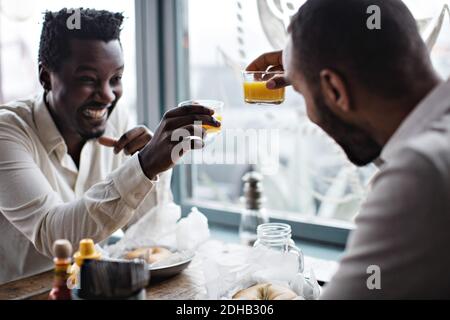 Happy friends toasting drinks while sitting at table in restaurant Stock Photo