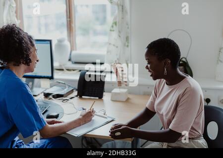 Smiling female nurse checking medical records while patient sitting at desk in doctor's office Stock Photo