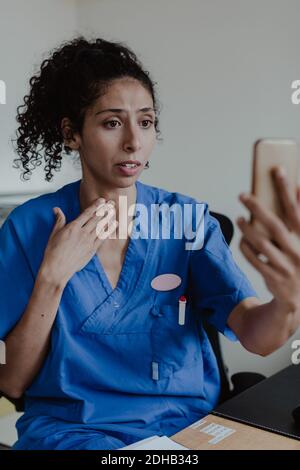 Worried nurse explaining on video conference while sitting in hospital Stock Photo