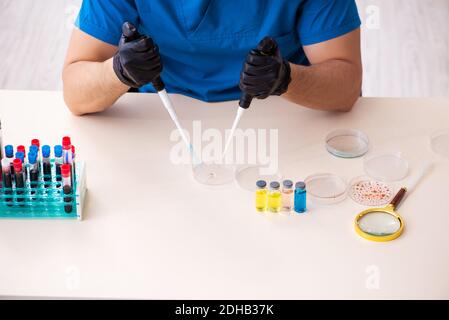 Young male biochemist testing blood samples in pandemic concept Stock Photo