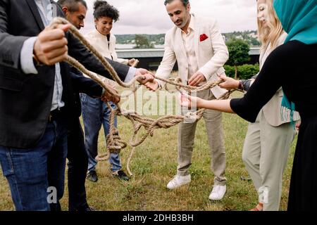 Multi-ethnic male and female colleagues holding rope while standing in lawn Stock Photo