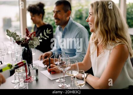 Smiling businesswoman looking away while sitting at table with colleagues in convention center Stock Photo