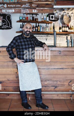 Full length of confident bartender standing by bar counter Stock Photo