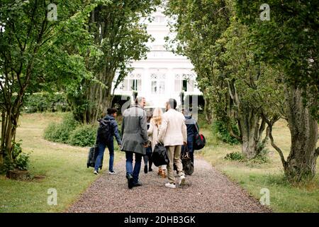 Rear view of male and female business professionals walking on footpath amidst trees Stock Photo
