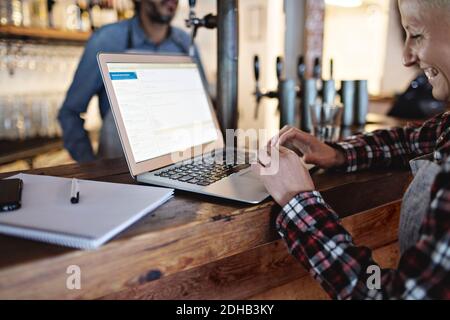 Smiling manager using laptop at bar counter Stock Photo
