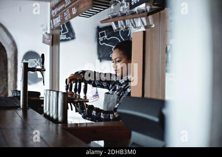 Female bartender pouring beer from tap at restaurant Stock Photo