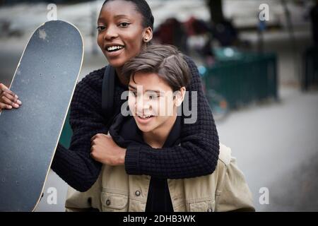 Young man piggybacking female teenage friend with skateboard Stock Photo