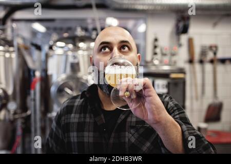 Male worker tasting craft beer while standing at factory Stock Photo