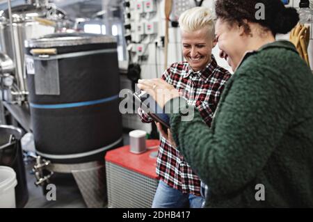Smiling female workers discussing over digital tablet while working in brewery Stock Photo