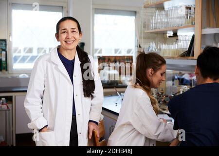 Portrait of confident mature female chemistry teacher standing by students in laboratory at university Stock Photo