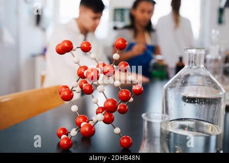 Molecular structure by glassware on table against young students in chemistry laboratory Stock Photo