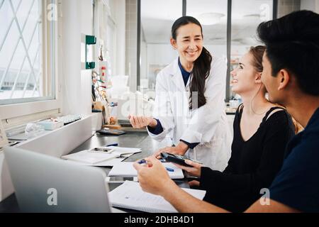 Smiling mature female teacher explaining to multi-ethnic young engineering students in university classroom Stock Photo
