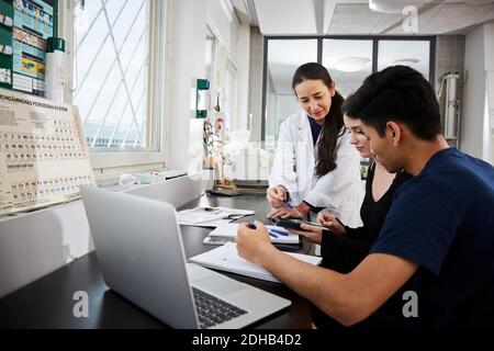 Mature female teacher explaining to multi-ethnic young university students in classroom Stock Photo