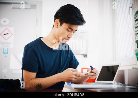 Confident young male university student using smart phone at classroom Stock Photo