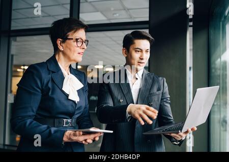 Young businessman discussing over laptop with senior coworker while standing in office Stock Photo