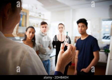 Rear view of mature female teacher holding test tube explaining to young multi-ethnic students in laboratory Stock Photo