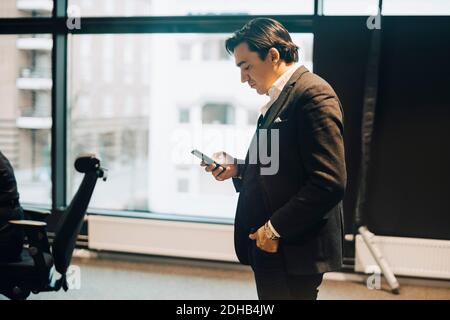 Side view of businessman using mobile phone while standing at workplace Stock Photo
