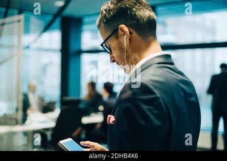 Mature businessman wearing headphones while using smartphone in office Stock Photo