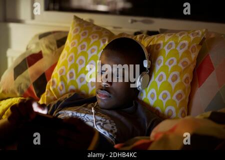 Close-up of boy with headphones using digital tablet while lying on bed at home Stock Photo
