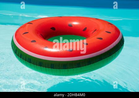 Inflatable watermelon patterned ring, floating in a swimming pool in the sun Stock Photo