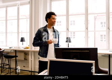 Male executive holding cup while looking away in office Stock Photo