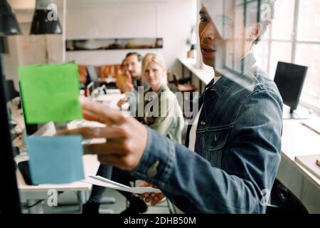 Businessman showing adhesive note to creative team seen from glass at workplace Stock Photo