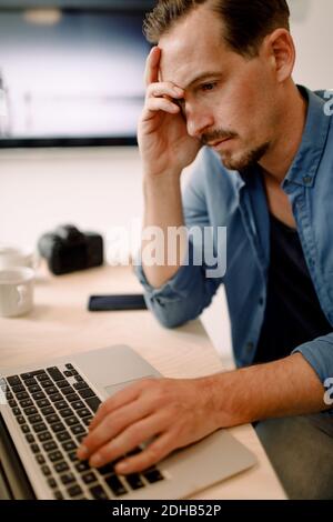 Worried businessman using laptop while sitting at creative office Stock Photo