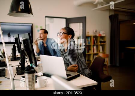 Smiling female colleague sitting by coworker at desk in workplace Stock Photo