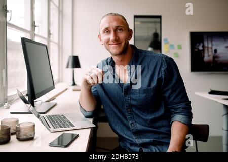 Portrait of young businessman sitting by office desk Stock Photo