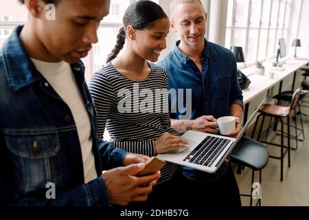 Smiling businesswoman discussing with colleagues over laptop in office Stock Photo