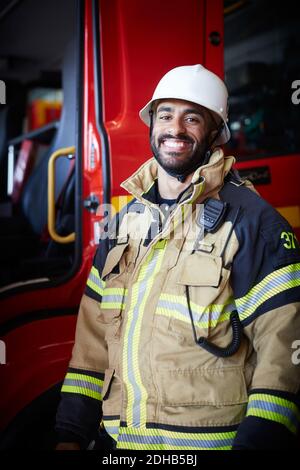 Portrait of smiling male firefighter standing against fire engine at fire station