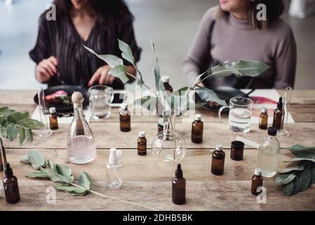 Midsection of young female colleagues sitting at table with various perfume bottles in workshop Stock Photo