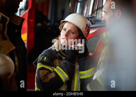 Female firefighter wearing helmet while talking with other coworkers in fire station Stock Photo