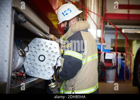 Side view of firefighter arranging fire hose in fire engine at station Stock Photo
