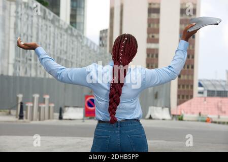 Happy businesswoman standing back with long red braids, holding a document with outstretched arms and relaxing outside offices feeling ecstatic on the Stock Photo