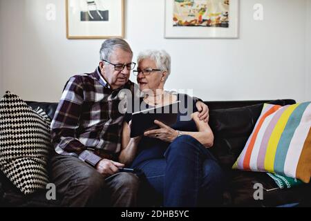 Senior couple sitting on sofa while sharing digital tablet against wall at home Stock Photo