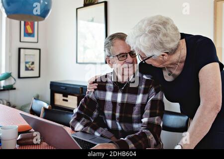 Smiling senior couple with laptop at dining table Stock Photo