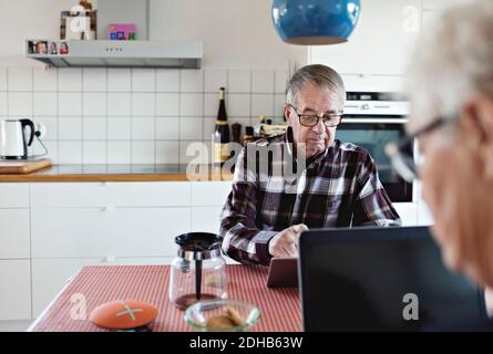 Senior couple using technologies sitting at dining table Stock Photo