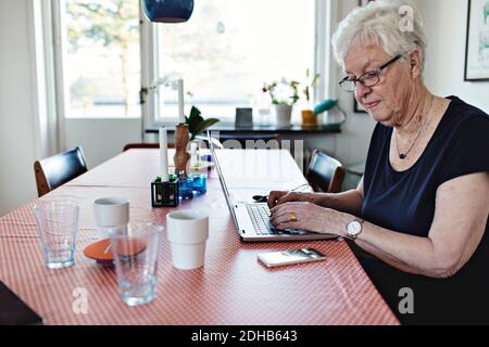Senior woman using laptop while sitting at dining table in room Stock Photo