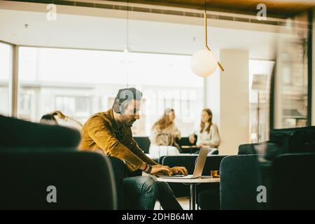 Side view of man wearing headphones and using laptop while sitting in restaurant Stock Photo