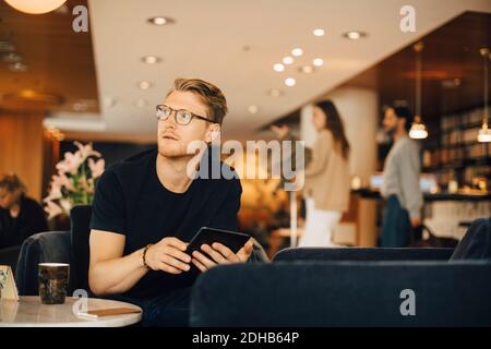 Thoughtful man looking away while using digital tablet in restaurant Stock Photo
