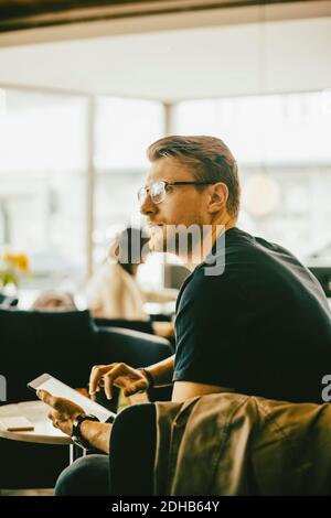 Mid adult man using digital tablet while looking away in restaurant Stock Photo