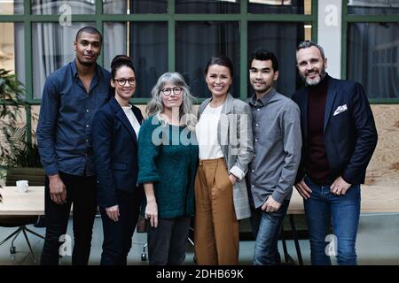 Portrait of confident smiling business team standing at table in creative office Stock Photo