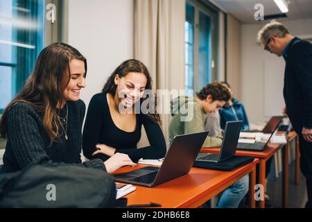 Cheerful female high school students using laptop at desk in classroom Stock Photo