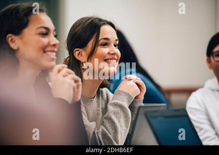 Smiling female students looking away while sitting in classroom Stock Photo