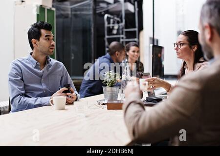 Business people having coffee while discussing in meeting at creative office Stock Photo