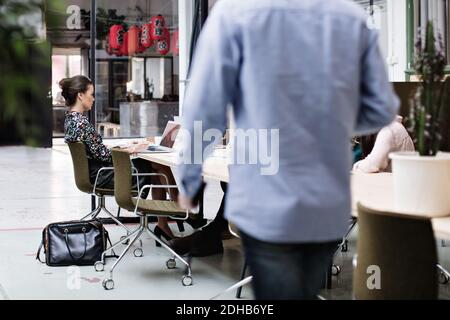 Businessman walking towards colleagues sitting at table in meeting Stock Photo