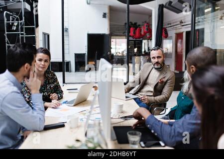 Business colleagues discussing in meeting while using technologies at creative office Stock Photo
